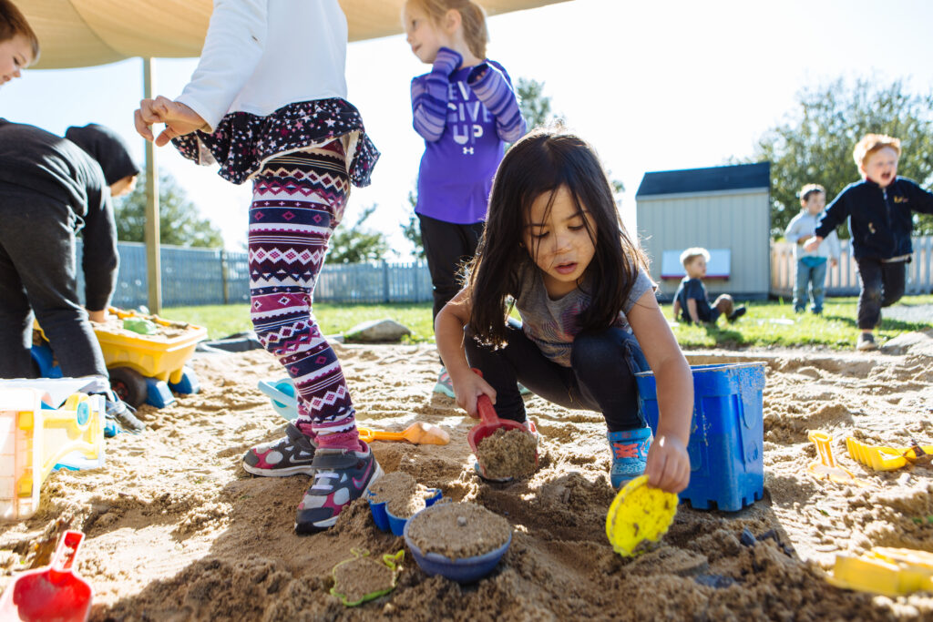 a child with long hair plays in the sand