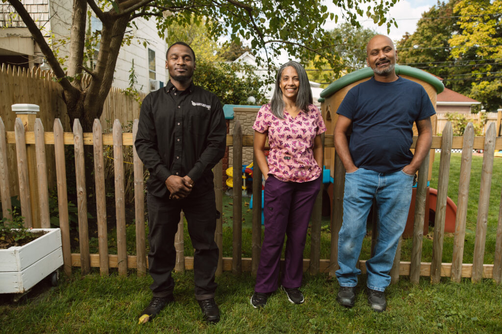 two men and a woman pose in front of a wooden fence