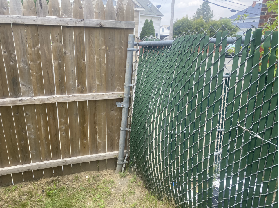 a chain link fence bulging where it meets a wooden fence