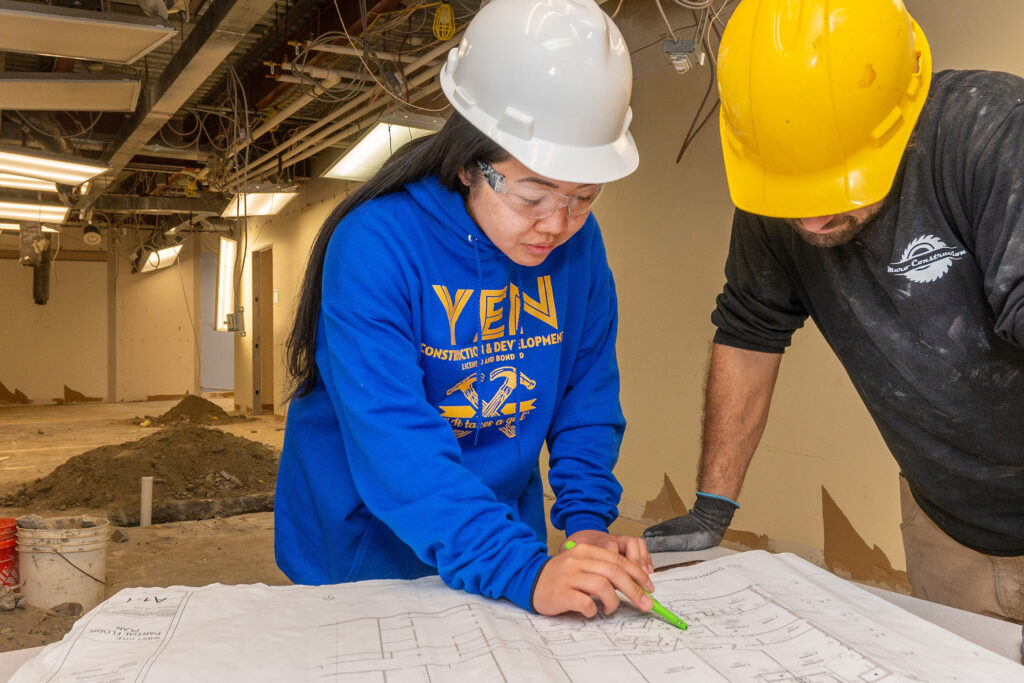 Two people in hard hats look at an architectural plan